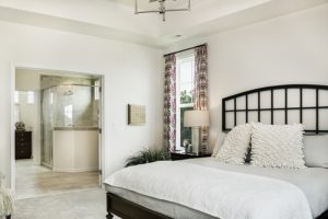Large king size bed with black headboard, decorative plant, curtains on window and attached bathroom.