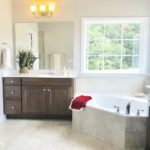Large custom designed bathroom with large tub underneath window, dark wood cabinets with sink and large mirror.