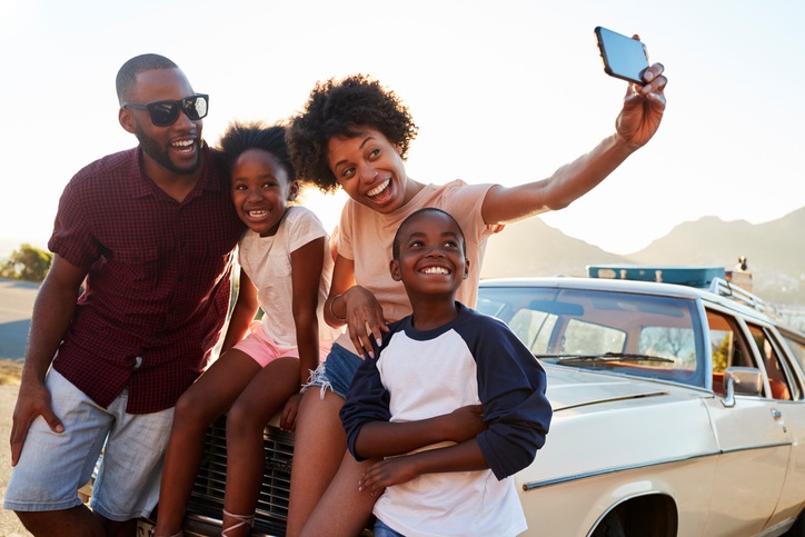 Family Posing For Selfie Next To Car Packed For Road Trip